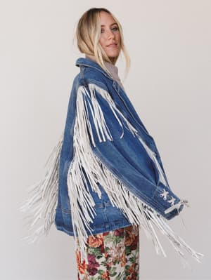 Woman wearing a blue denim jacket with white fringe on a plain background