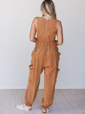 Back view of a woman wearing a rust sleeveless jumpsuit against a white background