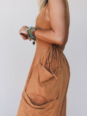 Rust sleeveless dress worn by a woman with colorful bracelets against a plain background