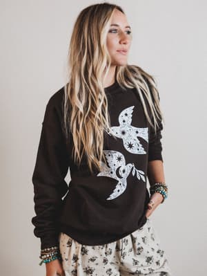 Woman wearing a black sweatshirt with white bird designs on a plain background