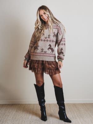 Woman wearing a patterned sweater and ruffled skirt with black knee-high boots against a plain background