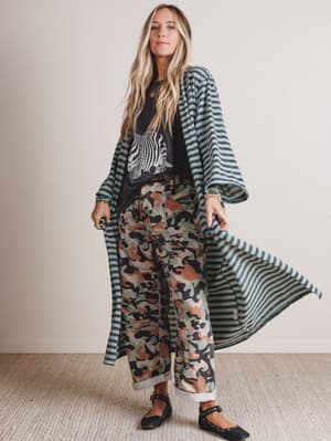 Woman wearing a long striped coat over a patterned outfit indoors.