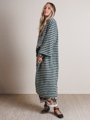 Woman wearing a long, dark green and white striped dress against a plain background