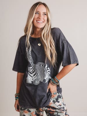 Woman wearing a black t-shirt with a zebra design and camouflage pants against a plain background