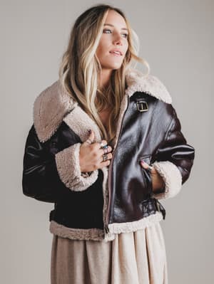 Woman wearing a black leather jacket with beige fur lining against a plain background
