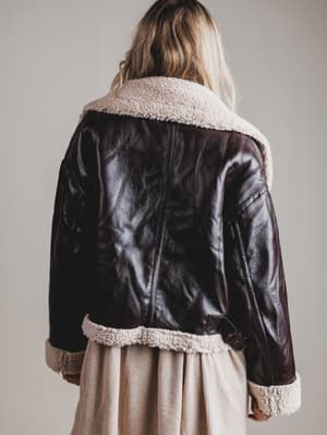 Person wearing a black leather jacket with white fur lining on a plain background