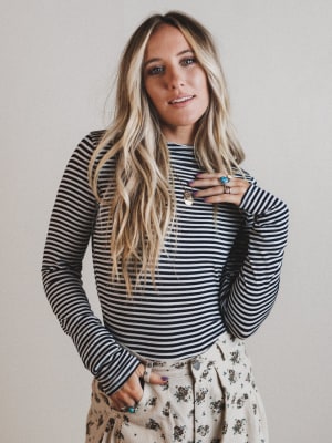 Woman wearing a striped long-sleeve top and floral pants against a plain background