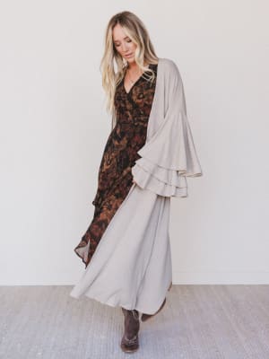 Woman wearing a patterned dress with a beige cardigan against a white background