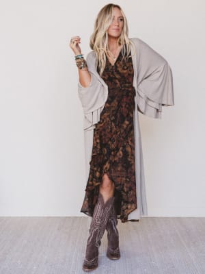 Woman wearing a patterned dress with a cardigan and boots against a white background