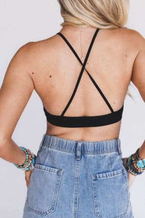 A woman with long blonde hair models the Crochet High Neck Bralette - Black, paired with high-waisted denim jeans and colorful beaded bracelets, posing with her back to the camera against a plain background.