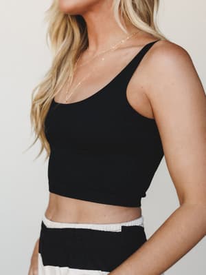 A cropped black ribbed bralette styled with a black-and-white striped bottom, layered gold necklaces adding a relaxed, collected feel against a soft neutral studio backdrop.
