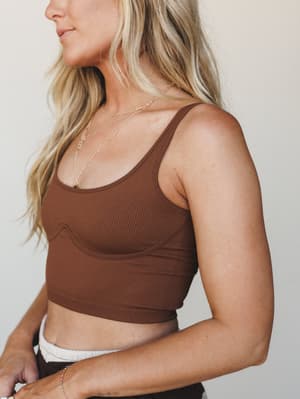 A ribbed brown crop bralette shot in close profile against a soft neutral wall — easy, effortless, and the kind of piece that layers under everything or stands on its own.