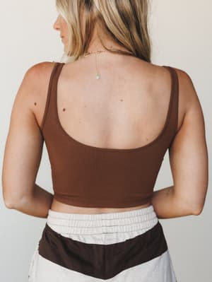 A back-facing shot of a ribbed brown crop bralette with a low scoop back, styled with color-block shorts and a delicate gold chain necklace — easy, laid-back, and quietly put-together.