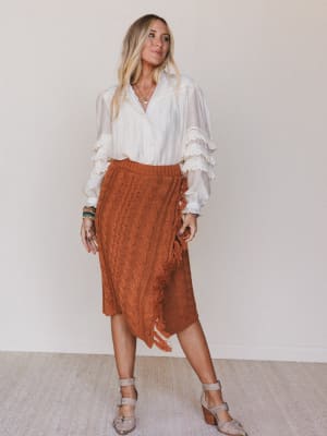 Woman wearing a white blouse and brown skirt against a plain background
