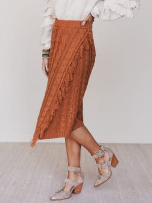 Person wearing a rust-colored lace skirt with a white blouse and beige sandals on a neutral background