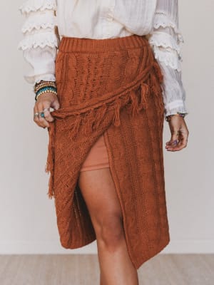 Person wearing a brown knitted skirt with tassels on a plain background