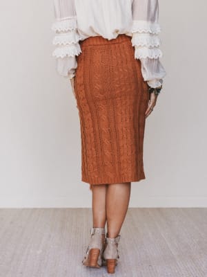 Person wearing a brown cable knit skirt with a white blouse against a neutral background