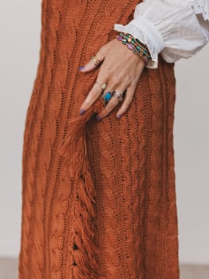 Close-up of a person wearing a rust-colored knitted sweater with a plain background