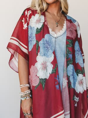 A flowy floral kimono in deep cranberry red layered over a chambray lace-trim camisole, styled with stacked beaded bracelets and a delicate gold pendant necklace — the kind of outfit that looks effortless but was definitely thought about.