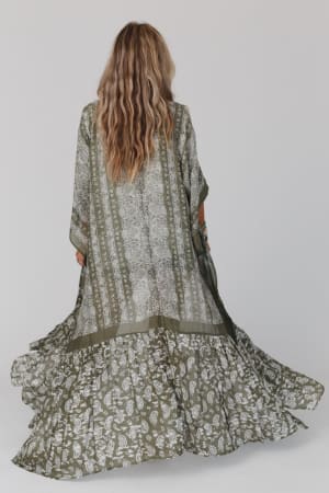 A woman with long wavy hair, seen from behind, wears the Paisley Tapestry Free Flow Duster Kimono in olive with white paisley and stripe patterns, set against a plain light background.