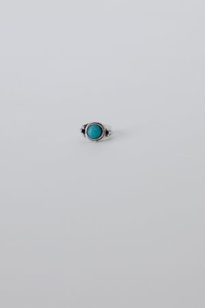 The Kapalua Bay Adjustable Turquoise Ring in silver, featuring a round turquoise stone at the center, rests on a light gray surface—an elegant piece for any jewelry collection.