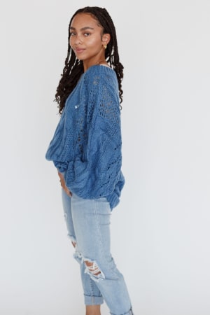 A woman with braided hair stands sideways, wearing the Golden Hour Bubble Sleeve Sweater Dress in blue, set against a plain white background.