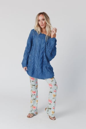 A woman with long blonde hair wears the Golden Hour Bubble Sleeve Sweater Dress in blue, posing against a plain white background with one hand raised and a relaxed expression.