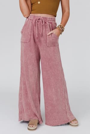 A woman wears Relaxing Robin Wide Leg Pant in New Mauve with a drawstring waist and large front pockets, paired with a brown sleeveless crop top, stacked bracelets, and tan platform sandals against a plain light background.