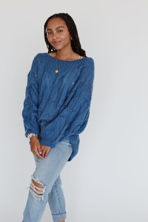 A woman with braided hair smiles slightly, standing against a white background in the Golden Hour Bubble Sleeve Sweater Dress - Blue, hands clasped in front of her.
