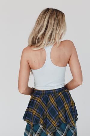 A woman with long blonde hair is shown from behind, wearing the High Neck Racerback Brami in light blue and a blue, green, and yellow plaid skirt against a plain, light background.