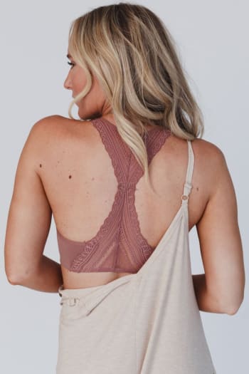 A woman with long blonde hair is seen from the back, wearing the Evermore Seamless Lace Racerback Bralette in mauve under a beige off-the-shoulder top that slips off her right shoulder to showcase the delicate bralette.