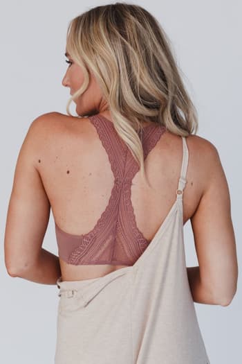 A woman with long blonde hair is seen from the back, wearing the Evermore Seamless Lace Racerback Bralette in mauve under a beige off-the-shoulder top that slips off her right shoulder to showcase the delicate bralette.