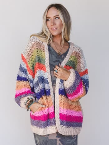 Woman wearing a colorful striped crochet cardigan over a camouflage patterned dress.