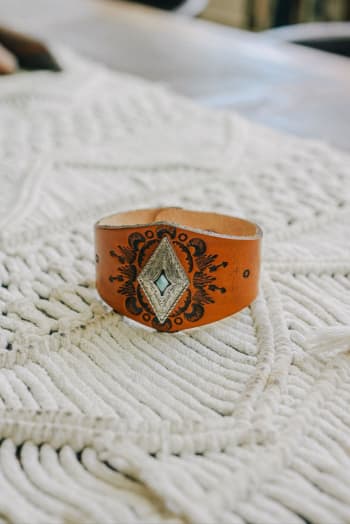 The Wynona Diamond Leather Cuff Bracelet - Camel features an intricate black and silver diamond-shaped design with a subtle turquoise accent, making it the perfect boho accessory for any outfit.