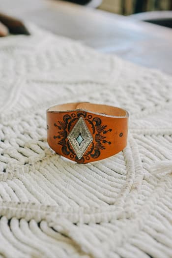 The Wynona Diamond Leather Cuff Bracelet - Camel features an intricate black and silver diamond-shaped design with a subtle turquoise accent, making it the perfect boho accessory for any outfit.