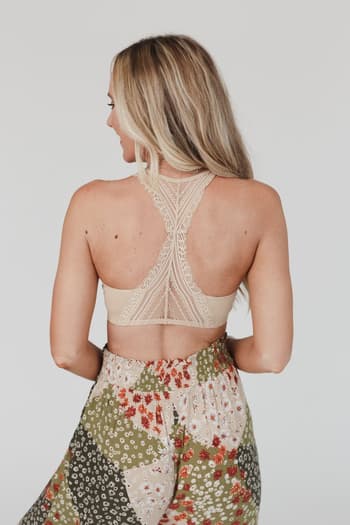 A woman with long blonde hair is seen from the back, wearing the Evermore Seamless Lace Racerback Bralette in beige and high-waisted floral patchwork pants. This chic layering piece pops against the plain white background.